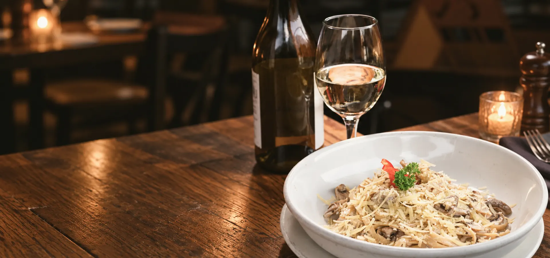 Plato de pasta con setas junto a una copa de vino blanco