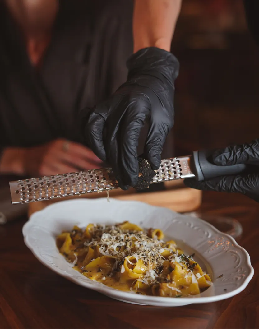 Cocinero rallando queso sobre un plato de pasta