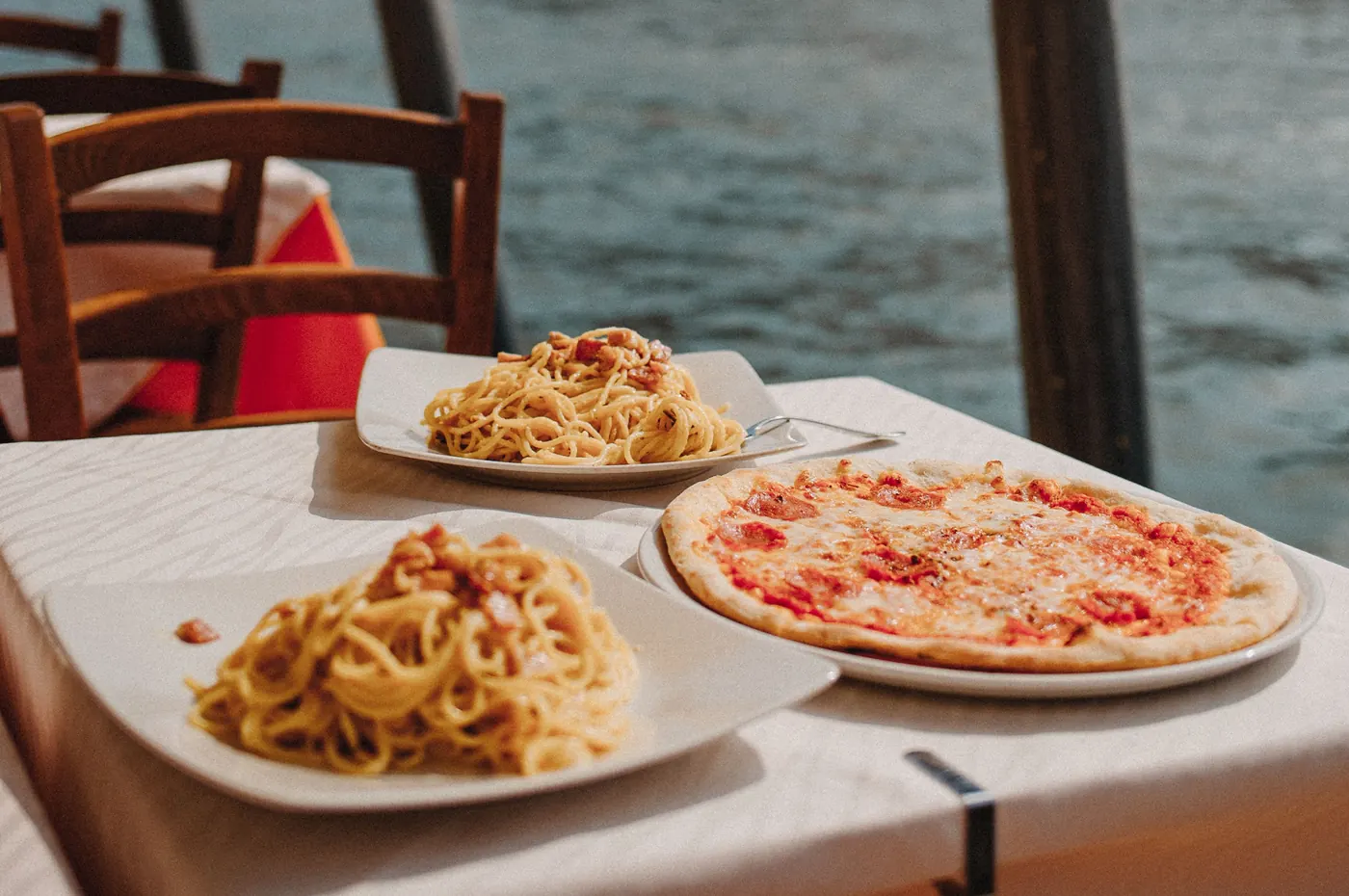 Mesa junto al mar con platos de pasta y una pizza